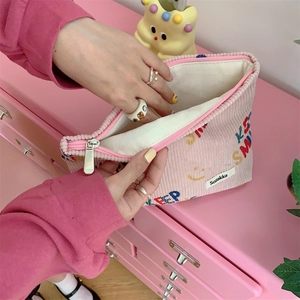Detailed view of pink corduroy pouch showing 'KEEP SMILING' embroidery and cream lining