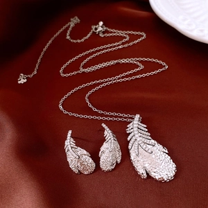 Detailed view of silver feather necklace and earrings set on dark red satin fabric