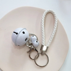 Detail of white bell keychain featuring woven rope and glossy metal lobster clasp on a plate