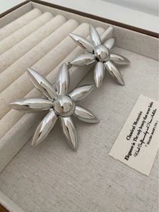 Macro detail of silver flower earrings with polished metallic finish in a beige jewelry box