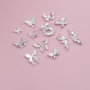 Macro shot of 12 silver hollow butterfly nail charms with rhinestones on pink background