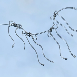 Detailed view of silver bow earrings with long tassels on a reflective surface