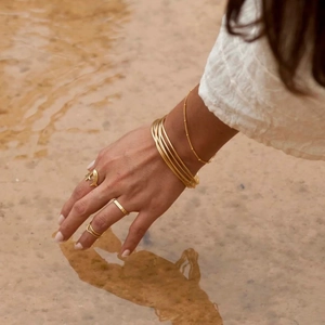 Close-up of gold star ring and stacked bracelets worn by hand over clear water
