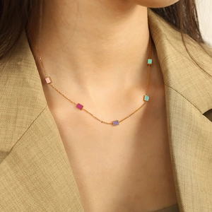 Elegant gold plated necklace with colorful square charms on a model in a beige suit