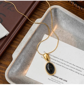 Macro shot of gold snake chain with oval black gemstone pendant on a vintage tray