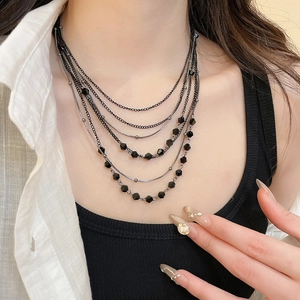 Detail of layered black crystal bead necklace showing mixed chains on a model