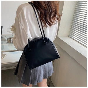 Model wearing a minimalist black leather shoulder bag with sleek dual straps and gold zipper