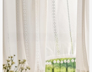 Close-up of white lace curtain featuring geometric diamond knit and soft pom-pom trim