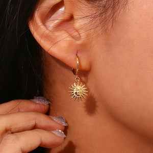 Close-up of a model wearing a gold sun charm earring with a detailed face design