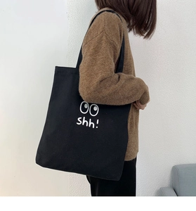 Foto de estilo de un bolso tote de lona negra con ojos de dibujos animados y diseño shh!
