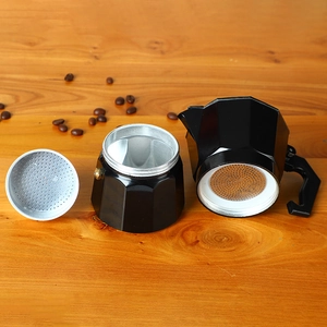Disassembled black aluminum moka pot parts on wooden surface with coffee beans