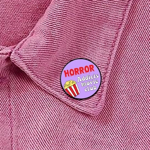 Macro detail of HORROR MOVIE LOVER enamel pin badge on a pink denim jacket collar