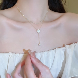 Detail of double-layer gold necklace with white camellia flower and pearl accents on model