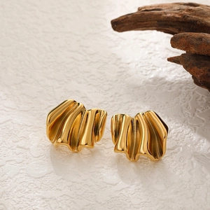 Macro detail of gold irregular wrinkled texture earrings on white stone background