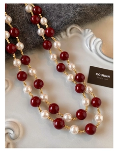 Dettaglio macro di perle rosse e bianche collegate da sottili maglie in metallo dorato