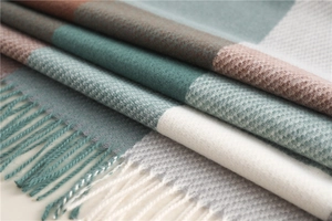 Macro detail of soft plaid scarf showing woven texture and decorative tassels in teal and brown