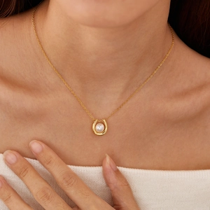 U-shaped gold pendant necklace with a pearl shown on a model neck close-up