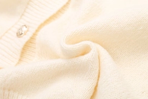 Gros plan détaillé du tissu en maille crème avec un bouton métallique sur le cardigan