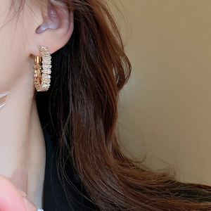 Close-up of gold hoop earrings with baguette-cut zircons worn by a model in warm light