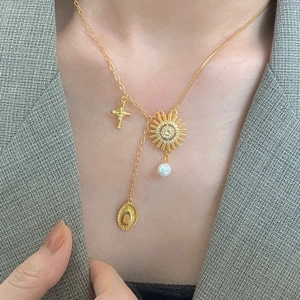 Detail of gold-plated 925 silver necklace with sun, cross, and pearl charms on a model