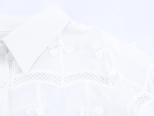 Dettaglio del colletto della camicia bianca con ricamo floreale e inserti in pizzo