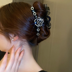 Détail d'une pince à cheveux avec nœud en résille noire, camélia en strass et pendentifs