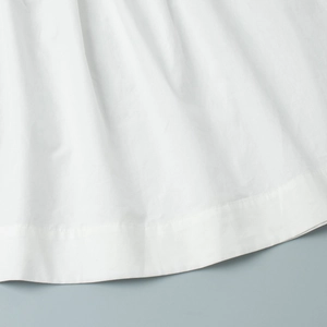 Détail du tissu en coton blanc montrant la texture plissée et l'ourlet piqué du short
