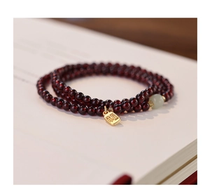 Detail of red garnet multi-wrap beaded bracelet with gold 'Fu' lucky charm on an open book