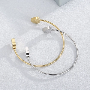 Polished gold and silver heart-shaped open bangles with geometric accents on white surface