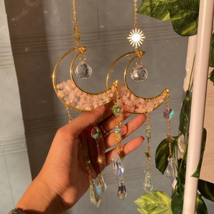 Detail of pink crystal moon suncatcher with gold metal frame casting rainbow light on wall