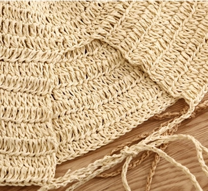 Close-up of beige straw sun hat showing intricate woven texture and decorative bow ribbon