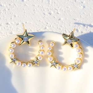 Close-up of gold-plated star and moon earrings with pearls and zircons on a white tray