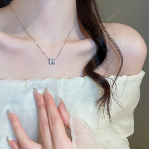 Close-up of silver-plated H-letter pendant necklace with zircons on a model's neck