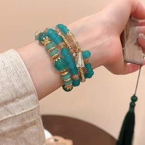 Detail of four-piece green crystal beaded bracelet set with gold alloy charms on wrist