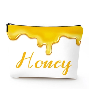 Close-up of white linen cosmetic bag with a golden honey drop design and zipper closure