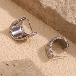 Macro shot of silver C-shaped earrings with micro-pave zircons on a rock background