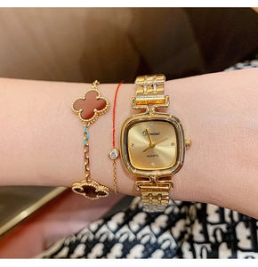 Close-up of gold square quartz watch worn with elegant red clover jewelry bracelets