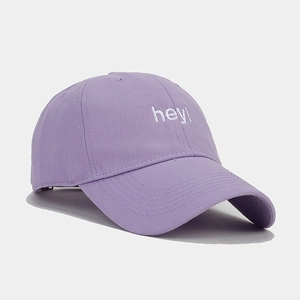 Detailed view of purple baseball cap featuring white 'hey!' embroidery and cotton twill texture