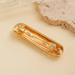 Detail of golden textured metal hair clip showing the spring closure mechanism
