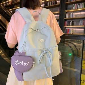 Pastel blue canvas backpack with purple heart charm shown on model in a library setting