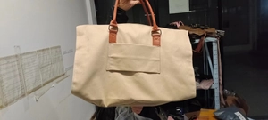 Détail du sac de voyage en toile beige avec poignées en similicuir marron et poche avant