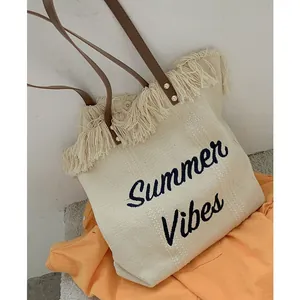 Detail of woven tote bag with Summer Vibes embroidery and brown leather shoulder straps