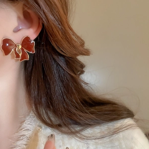 Detail of red bow earring with gold edges worn by a model in a warm-toned side view close-up