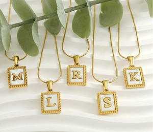 Detail of 18K gold snake chain necklaces featuring square white initial pendants