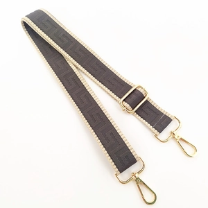 Detail of adjustable woven bag strap with geometric patterns and gold metal buckles