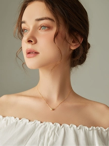 Close-up of golden bean pendant on a fine chain worn by a model in warm lighting
