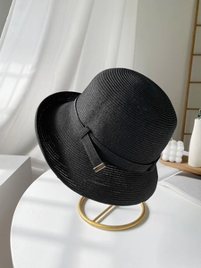 Dettaglio cappello di paglia nero con trama a spirale su supporto minimalista dorato