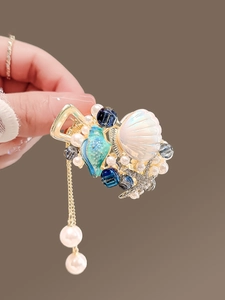 Détail d'une pince à cheveux dorée avec coquillage océanique et pampilles de perles