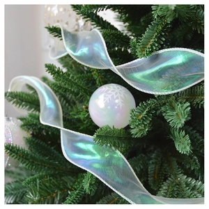 Iridescent ribbon and white snowflake ornament hanging on a lush green Christmas tree