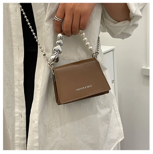 Detailed close-up of a brown mini bag with heart and pearl chain handle on a model